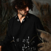 Man wearing a black shirt with white patterns sitting in a natural setting