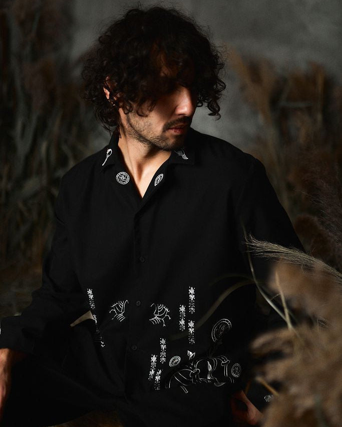 Man wearing a black shirt with white patterns sitting in a natural setting