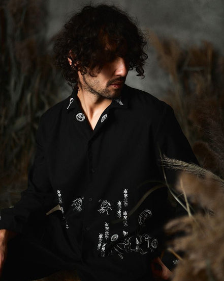 Man wearing a black shirt with white patterns sitting in a natural setting