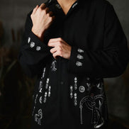 Man wearing a black shirt with white embroidery against a dark background