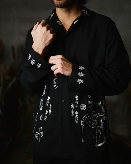 Man wearing a black shirt with white embroidery against a dark background