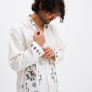 Man wearing a white embroidered shirt against a white background