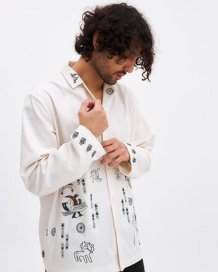 Man wearing a white embroidered shirt against a white background