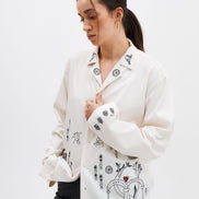 Woman wearing a white jacket with black embroidered designs on a plain background