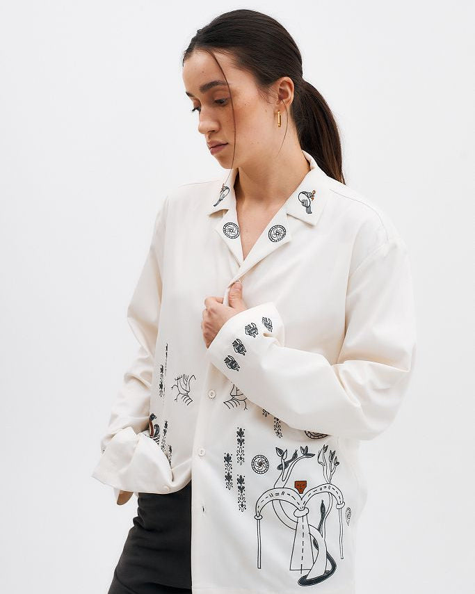 Woman wearing a white jacket with black embroidered designs on a plain background