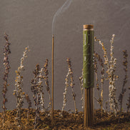 Cigarette with a lit end surrounded by small plants on a gray background