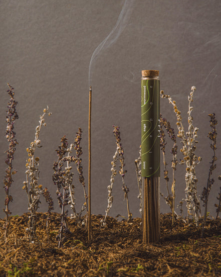 Cigarette with a lit end surrounded by small plants on a gray background
