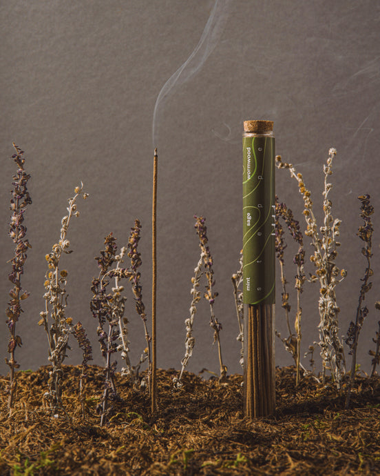 Cigarette with a lit end surrounded by small plants on a gray background