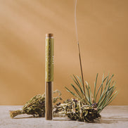 Incense stick with green wick and dried herbs on a wooden surface against a beige background