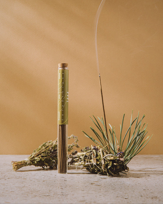 Incense stick with green wick and dried herbs on a wooden surface against a beige background