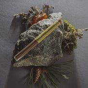 Metallic pen on a rock with natural elements against a dark background