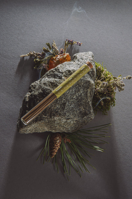 Metallic pen on a rock with natural elements against a dark background