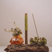Incense stick with a decorative stone and herbs on a wooden stand against a plain background