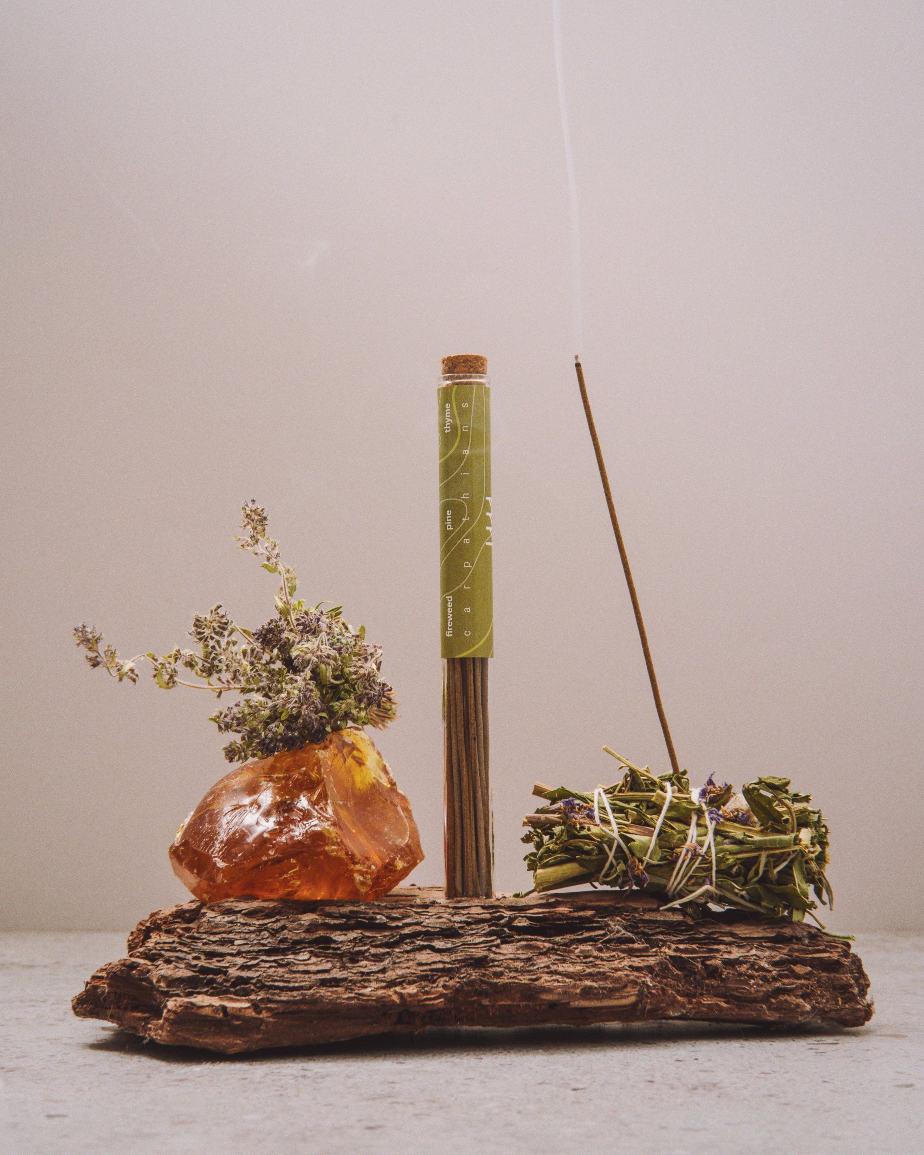 Incense stick with a decorative stone and herbs on a wooden stand against a plain background