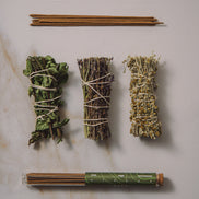 Three bundles of dried herbs tied with twine on a marble surface, with a tube of incense sticks.