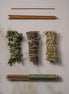 Three bundles of dried herbs tied with twine on a marble surface, with a tube of incense sticks.