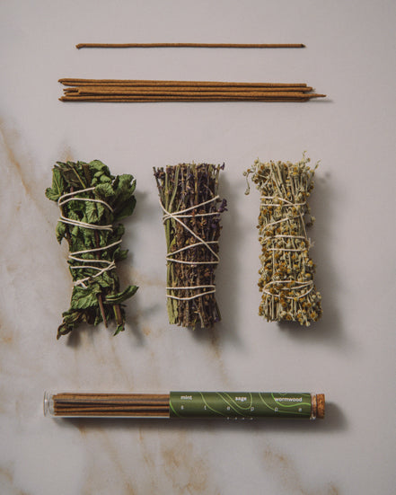 Three bundles of dried herbs tied with twine on a marble surface, with a tube of incense sticks.