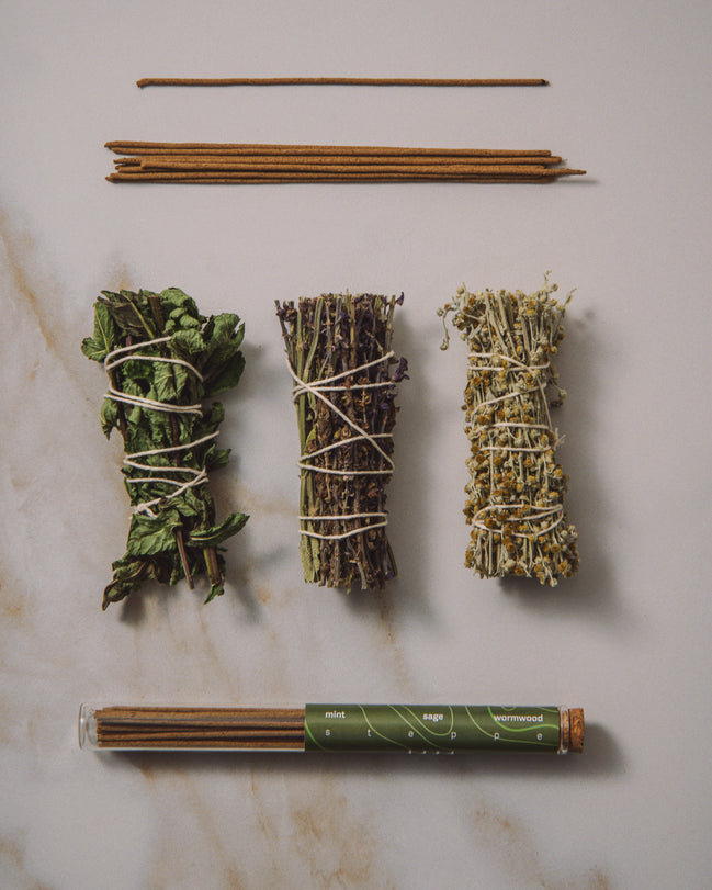 Three bundles of dried herbs tied with twine on a marble surface, with a tube of incense sticks.