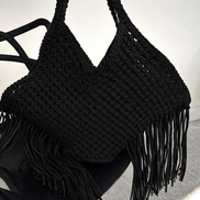 Black woven handbag with fringe on a black chair against a white background