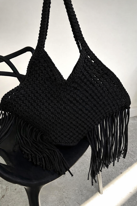 Black woven handbag with fringe on a black chair against a white background