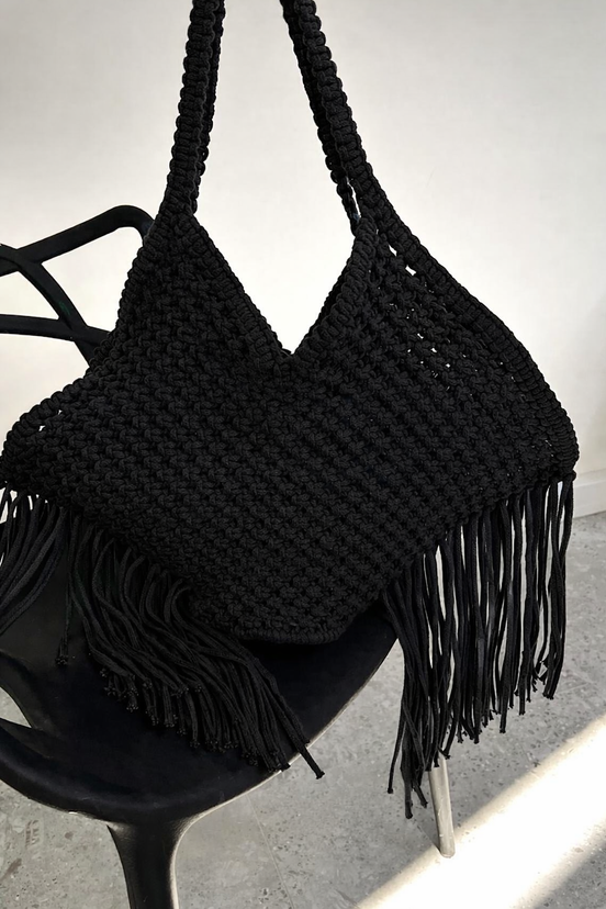 Black woven handbag with fringe on a black chair against a white background