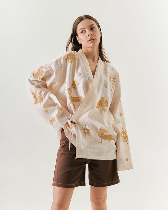 Woman wearing a white kimono with gold patterns on a plain background