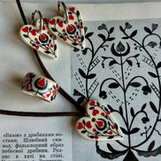 Heart-shaped ceramic earrings with red and black patterns on a piece of paper with black line art.