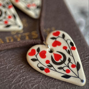 Heart-shaped ceramic ornament with red and black patterns on a textured surface