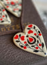 Heart-shaped ceramic ornament with red and black patterns on a textured surface