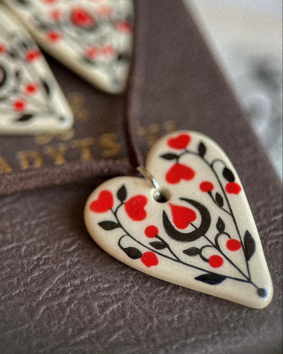 Heart-shaped ceramic ornament with red and black patterns on a textured surface