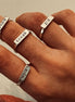 Hand wearing multiple silver rings with engraved text.