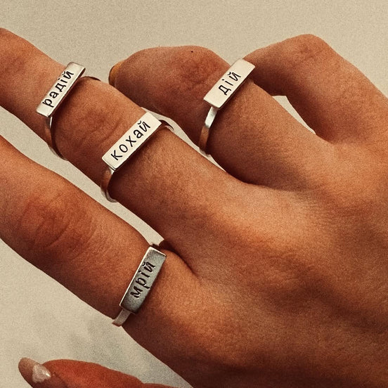 Hand wearing multiple silver rings with engraved text.