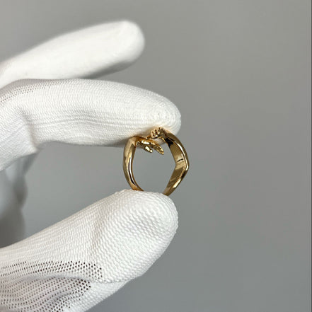 Gold ring held by a gloved hand against a gray background