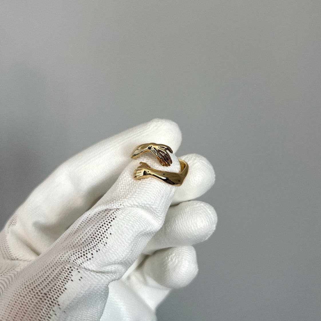 Gold ring held by a white-gloved hand against a gray background
