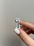 Hand holding a small letter 'i' charm against a neutral background