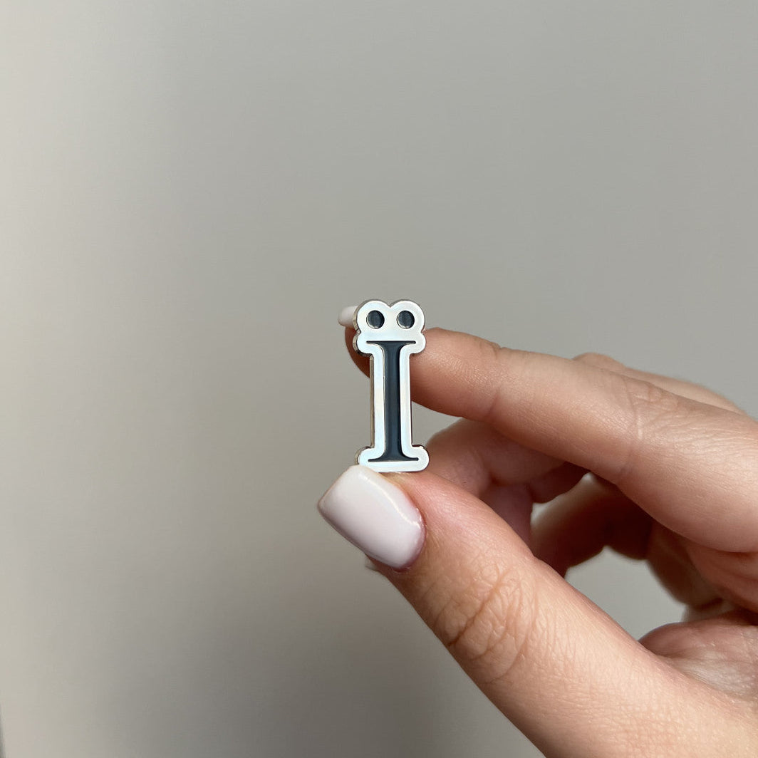 Hand holding a small letter 'i' charm against a neutral background
