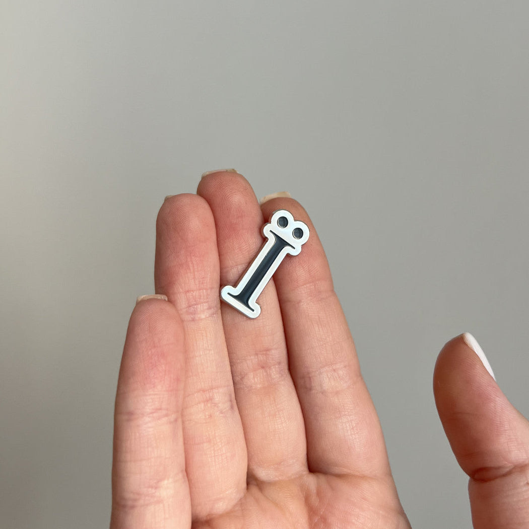 Hand holding a small white sticker with a black letter '
ї' on a gray background