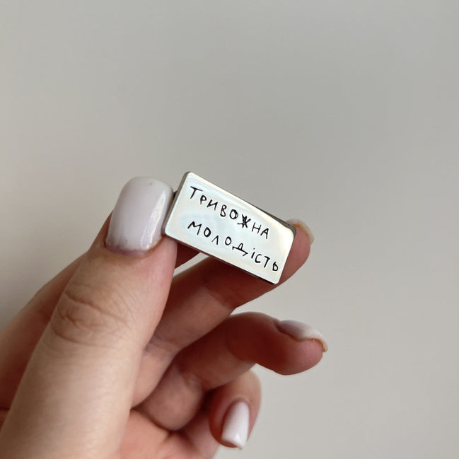 Hand holding a small rectangular metal object with engraved text on a plain background