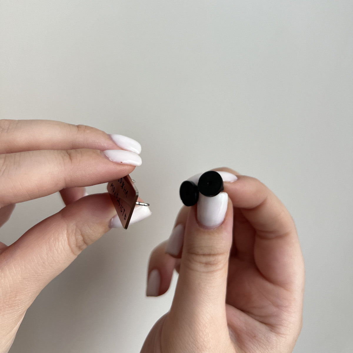 Close-up of a hand holding two small objects against a plain background