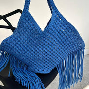 Blue woven handbag with fringe on a black chair against a white background