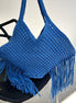 Blue woven handbag with fringe on a black chair against a white background