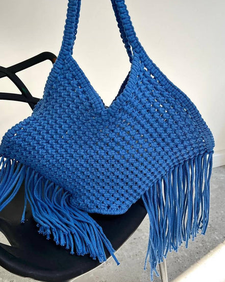 Blue woven handbag with fringe on a black chair against a white background