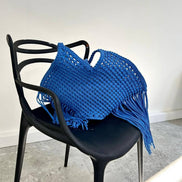 Blue woven bag with fringe on a black chair against a white wall.