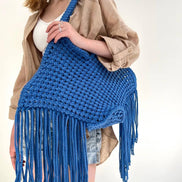Person holding a blue crocheted bag with fringe against a white background