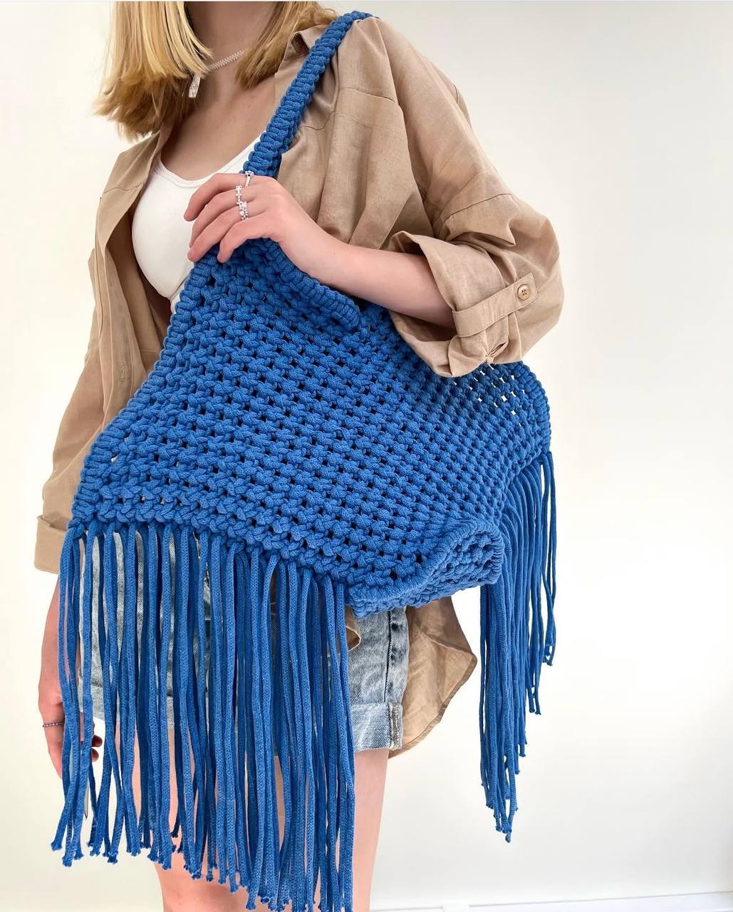 Person holding a blue crocheted bag with fringe against a white background