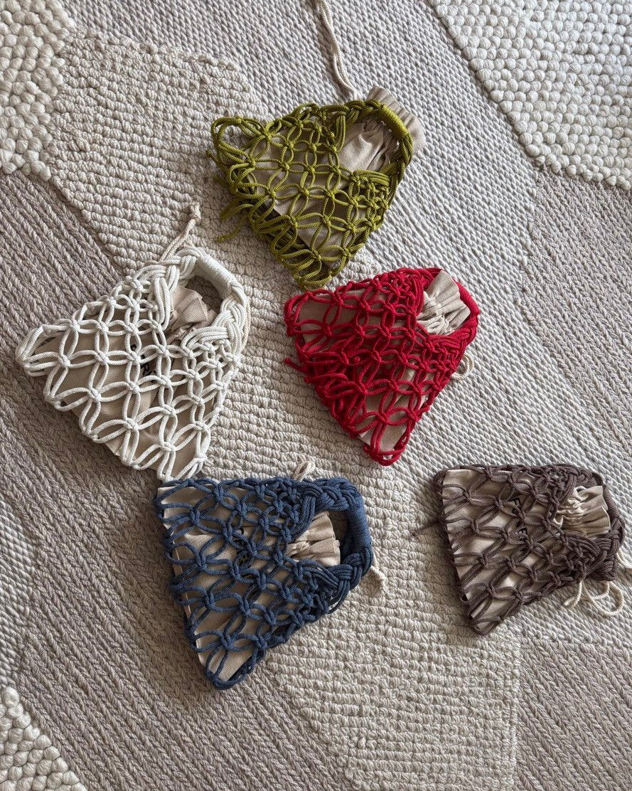 Five small woven bags in different colors on a textured fabric background