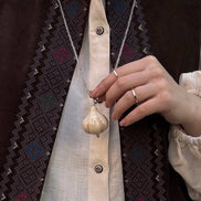 Person wearing a vest with intricate patterns and holding a necklace.
