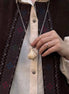 Person wearing a vest with intricate patterns and holding a necklace.