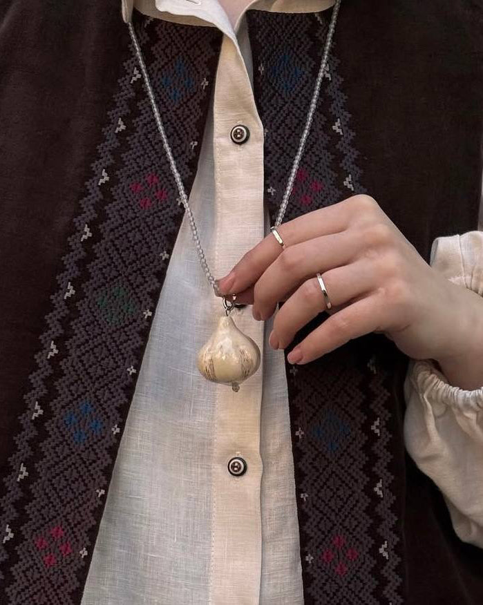 Person wearing a vest with intricate patterns and holding a necklace.