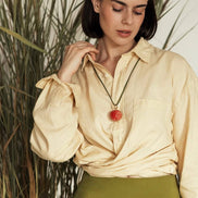 Woman wearing a beige blouse with a red pendant necklace in front of tall grass.